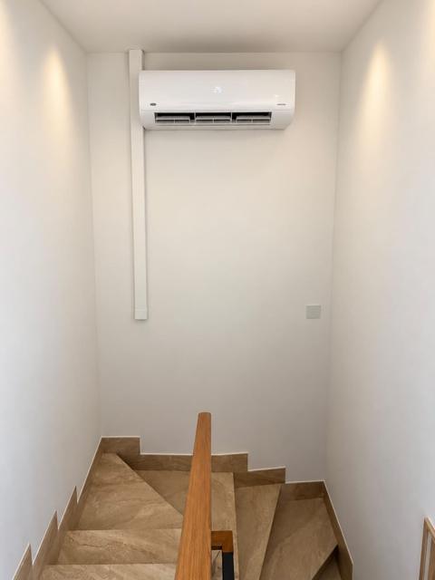 Nástěnná klimatizace nad schodištěm s lištou vedenou po stěně